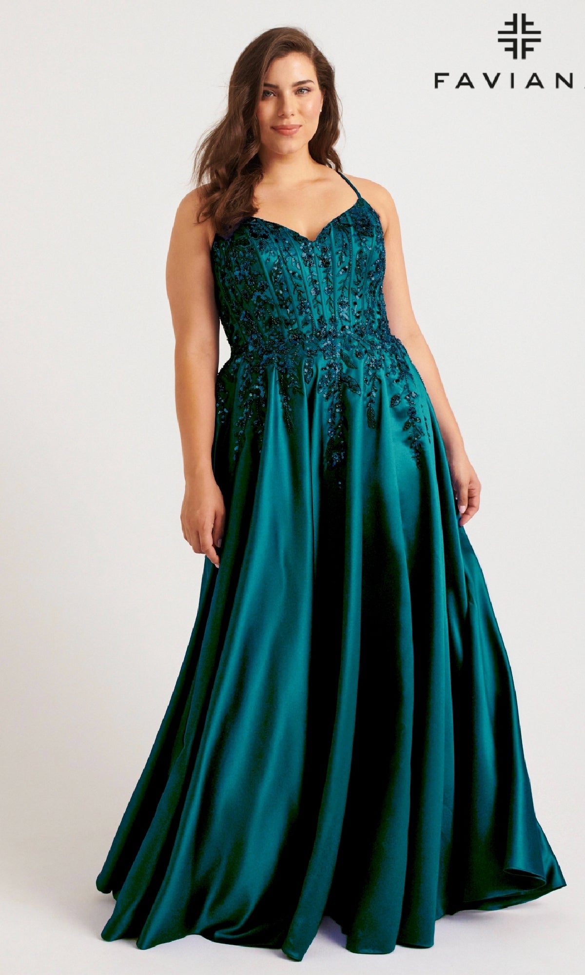 A woman wears the Faviana 9575 long plus-size prom dress in deep teal, featuring a fitted embroidered bodice and flared satin skirt. The Faviana logo appears in the top right corner.